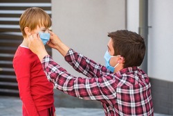 Father puts a medical mask on her son. Coronavirus, illness, infection, quarantine, medical mask, COVID19. Father, child wear facemask during coronavirus, flu outbreak. Dad with a son in medical mask.