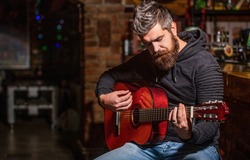 Live music. Guitars and strings. Bearded man playing guitar, holding an acoustic guitar in his hands. Music concept. Bearded guitarist plays. Play the guitar. Beard hipster man sitting in a pub.