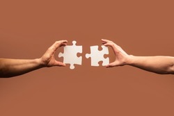 Two hands trying to connect couple puzzle piece on gray background. Teamwork concept. Closeup hand of connecting jigsaw puzzle.