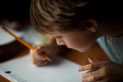 A cute little boy writing with a pencil close up