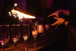 Closeup girl bartender pours champagne into glasses. Rest in a nightclub, pub, restaurant. Decorative firework sparkling column of fire on a bottle of champagne