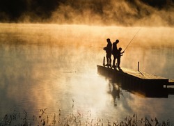 Early morning fishing in autumn on a lake as the mist rises from the water.