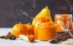Canned organic pumpkin puree in glass jar with fresh pumpkin, cinnamon and anise on light background. Ingredient for Thanksgiving, autumn or winter recipes.