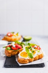 Variety of croissant sandwiches with tomato, cucumber, mozzarella cheese, eggs and mashed avocado with mint and arugula. Open savory sandwiches. Tasty healthy breakfast.