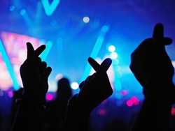 K-Pop music theme or Live concert background with silhouette hands of audience making mini heart shaped hand gesture for artist supporting on blurred background of audience and stage with neon light.