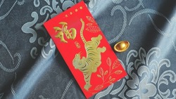 Chinese Lunar New Year red envelope with the tiger and blessing words contained money as a gift on brocade fabric with ancient gold bullion nugget. The Chinese word means happiness and good fortune.