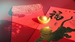 Chinese Lunar New Year ancient gold bullion nugget over red envelopes with the tiger and blessing words contained money as a gift on red background. The Chinese word means happiness and good fortune.