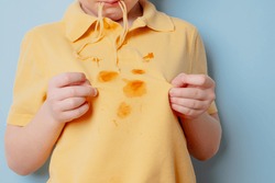 Ketchup stains on a yellow t-shirt. Hungry boy licking snack from his fingers. isolated on blue background. High quality photo