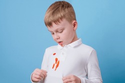 Boy showing a red stain spilled from tomato sauce on white clothes. The concept of cleaning stains on clothes. High quality photo