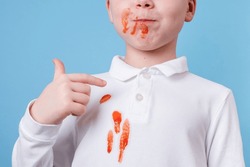 Close up stain tomato sauce spilling on white clothes. the child fingers tastes the tomato sauce. daily life stain concept. 