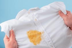 Dirty yellow stain on a white shirt. men's hands showing and visual evaluation of stain. Spoiled linen. isolated. top view. High quality photo