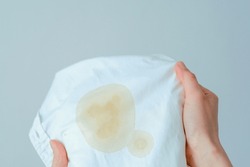 Hand showing dirty souce cosmetic stain on white shirt. Visual evaluation of stains on clothes. Liquid yellow stains. daily life stain concept. High quality photo