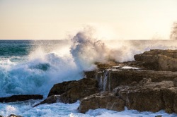Big wave crashes against the rocks of a coast in the sunlight