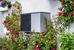 Outdoor unit of heat pump heating of residential house framed by roses