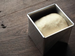 proofing white bread dough in square tin mold on wooden table