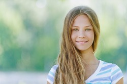 Beautiful smiling teenage girl in blue blouse, against green of summer park.