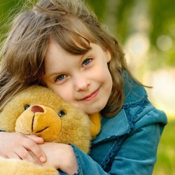 The small beautiful girl embraces an amusing bear cub against the summer nature.
