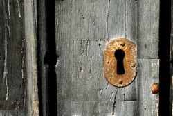 A close up of an old rusty metal keyhole on an old wooden door 