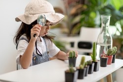 kid gently touch new stem of the cactus he grows with care, one hand holds magnifying glass.Nature education, Montessori and observation skills concept.