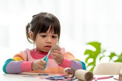Portrait of a little asian girl cutting a paper in activities on DIY class at School.Scissors cut paper.