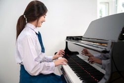 Female pianist in uniform playing classic grand piano in the school. Professional musician young woman happy and feeling relax during practice piano. Online music school business. Natural movement