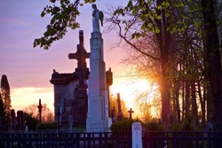 Statue of an angel and silhouettes of crosses and trees against sky at sunset in an old Christian cemetery