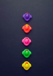 Colorful rubber ducks aligned in a line over dark grey background, above view
