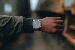 Close-up of a watch with a brown leather strap on an African American hand. Blurred background. Isolated object on bokeh background