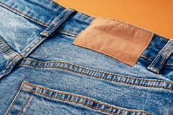 Blue jeans with a brown leather blank label, close-up. Jeans texture. Fashion denim background for sewing, copy space. Label on clothing for indicate the size, company.