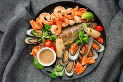 Roasted Mixed Seafood Contain Mussels, prawns, salmon, Calamari Squids and Grilled Barracuda Fish Garlic with Spicy Chili Sauce. Isolated on gray Background. Seafood and meat platter. Mediterranean