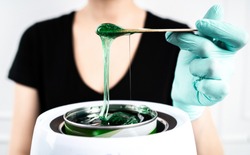 The concept of depilation and beauty is sugar paste or hair removal wax. Preparation of green wax for sugaring. Close-up sugar paste or wax honey for hair removing with wooden waxing spatula sticks.