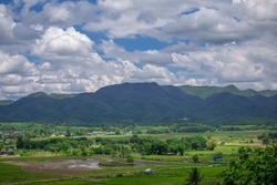 A bird's-eye view of a small village in the countryside Surrounded by mountains and nature in the rainy or farming season of Lampang Province, Thailand.