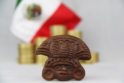 Coins of ten Mexican pesos with figure of the Aztec culture and Mexican flag in the background
