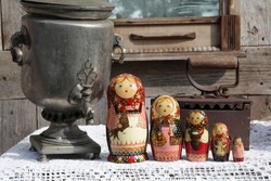 Russian traditional wooden nested dolls, matryoshka, in form of women in national costumes. Ancient iron, antique silver samovar for tea drinking. Russian style in folk art, handicraft, ethnic craft