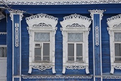 Ornamental windows with carved frames on vintage blue wooden rural house in Maydakovo village, Ivanovo region, Russia. Building facade. Russian traditional national folk style in wooden architecture