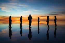 Diverse group of travellers silhouetted against sunrise at Uyuni Salt Flats (Spanish: Salar de Uyuni ) in Bolivia, South America.