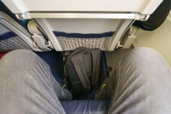 In the cabin of the low-cost airline. Male legs. Wearing jeans. Backpack.