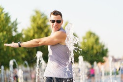 Handsome man hitting cold water of fountains in the hot summer day in the big city. Fresh water splashes. Concept of the leisure time, freshness and happiness. Portrait, frontal view