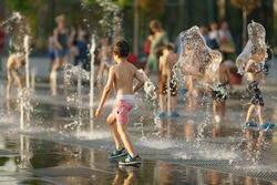 Child playing with water of fountain. He having fun walking through the fountain. Hot summer amusement. Leisure concept. Back, rear view