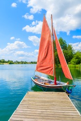 Small traditional sailing boat mooring at wooden pier on Kryspinow lake marina on sunny summer day, Poland