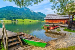 Fishing boats and wooden house on shore of Weissensee lake in summer landscape of Carinthia land, Austria