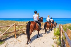 Young women riding horses to sandy beach in Lubiatowo coastal village, Baltic Sea, Poland