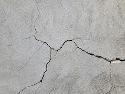 Cracked concrete wall covered with gray cement mortar. Destruction caused by an earthquake. Large uneven crack in the wall. Copy space. Texture background. Repair, construction of buildings, shrinkage