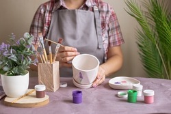 Women in gray apron paint a white flower ceramic pot