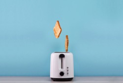Roasted toast bread popping up of stainless steel toaster on a blue backgroun. Space for text