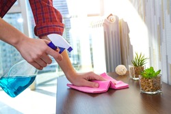 A housewife in a shirt cleans the house, wipes dust from the table with a cleaning rag and a spray. Household chores