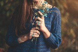 Boho chic woman in knitted blue sweater and wearing silver rings with turquoise stone with bouquet of wildflowers in hands in autumn forest outdoors in fall. Jewelry girl with boho fashion