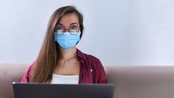 Business woman in round glasses wears medical protective mask working from home at the computer during self-isolation and quarantine. Coronavirus outbreak and covid epidemic. Stay home. Copy space