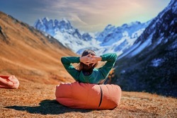 Wanderer girl sitting on soft chair during resting in a camping. Traveler enjoying scenic landscape while traveling in a mountain valley