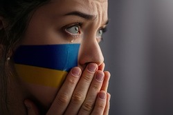 Crying sad feared depressed frightened emotional woman with Ukraine flag on face in the dark. Stop war between Russia and Ukraine. Stay with Ukraine. Pray and hope for peace and world. Copy space 